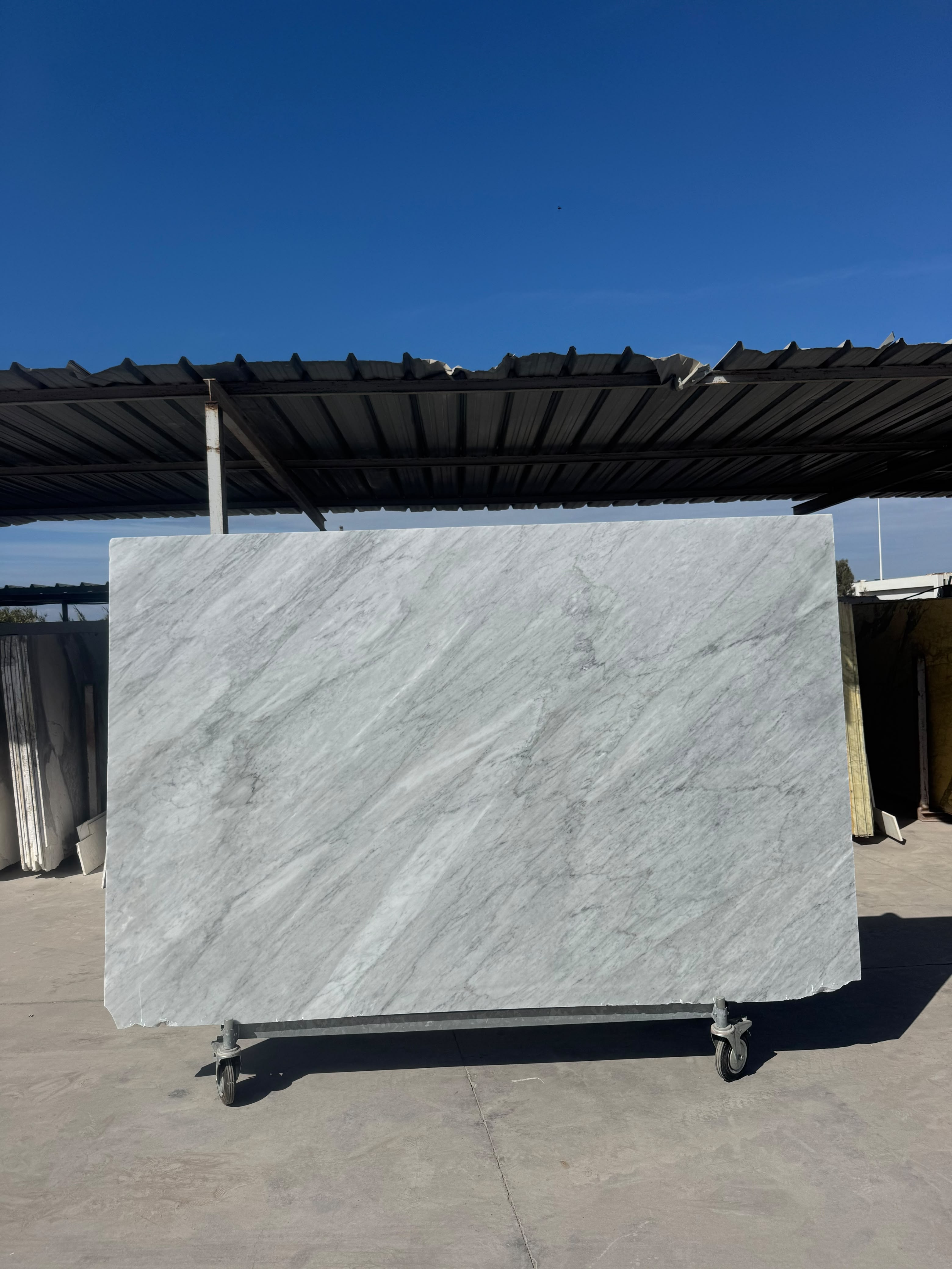 Dalle Blanc Carrare — marbre blanc italien au fond blanc grisé, parcouru en diagonale par des traînées claires, des nuages gris et de fines veines grises