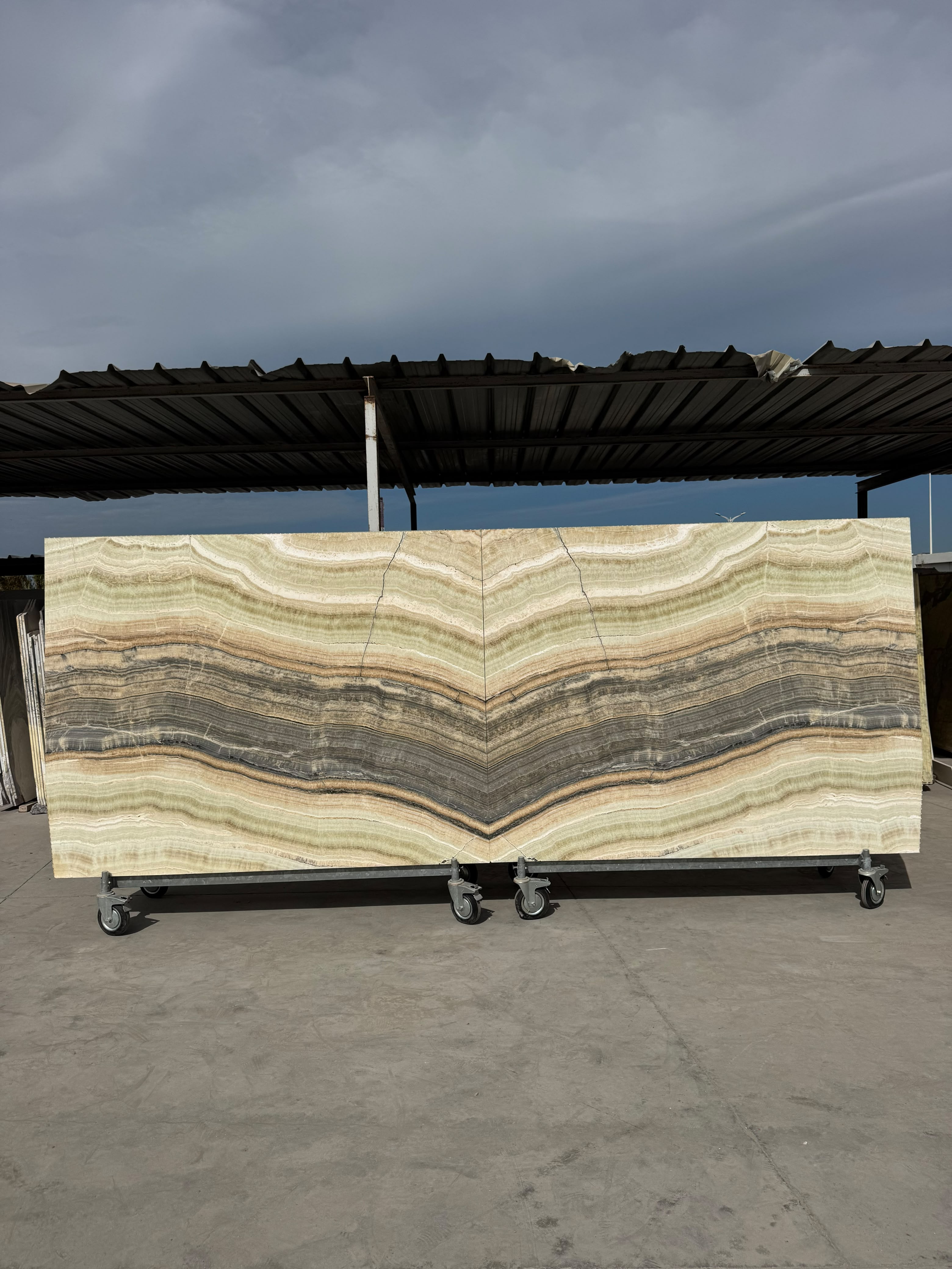 Deux dalles Onyx Miel en book-match sur chariot au dépôt ARCHIMAR de Temara — onyx turc rubané de vert pâle, de miel et de gris, dont les bandes se répondent en miroir et dessinent un grand chevron